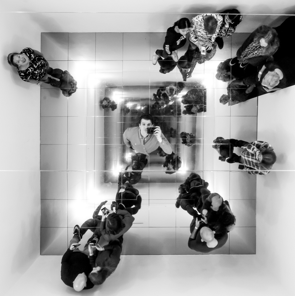 Edouard Schneiders photographed in a mirrored installation, camera raised, among other visitors